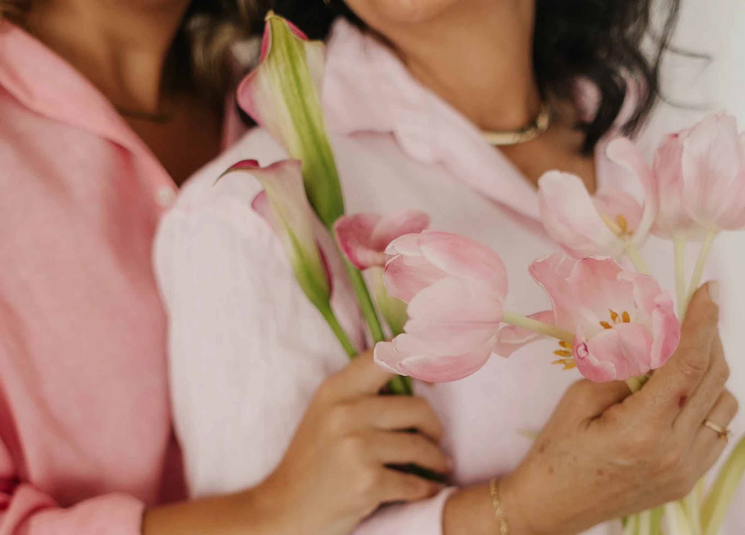 Mãe e filha lado a lado segurando tulipas e copos-de-leite rosa